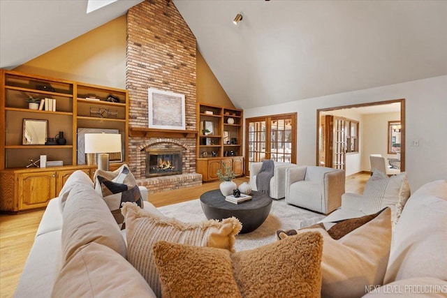 living area with light wood-style floors, a brick fireplace, high vaulted ceiling, and built in shelves