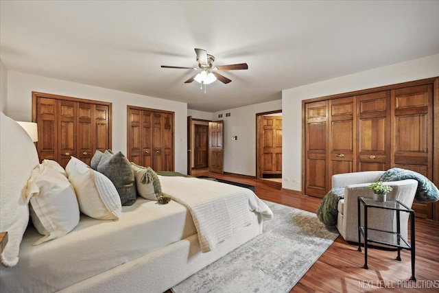 bedroom featuring a ceiling fan, multiple closets, and wood finished floors