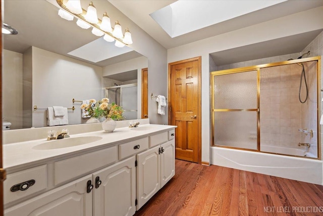 bathroom with a skylight, wood finished floors, a sink, combined bath / shower with glass door, and double vanity