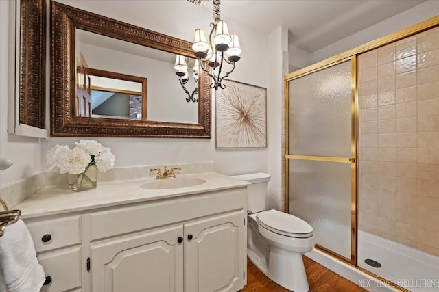 bathroom with a chandelier, toilet, wood finished floors, vanity, and a shower stall