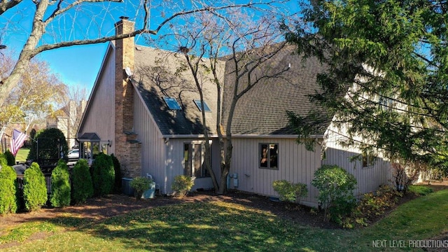 exterior space featuring a shingled roof, a chimney, and a front lawn