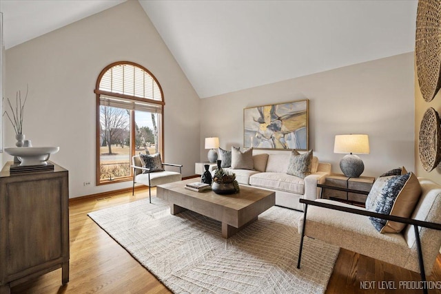 living room featuring light wood finished floors, baseboards, and high vaulted ceiling