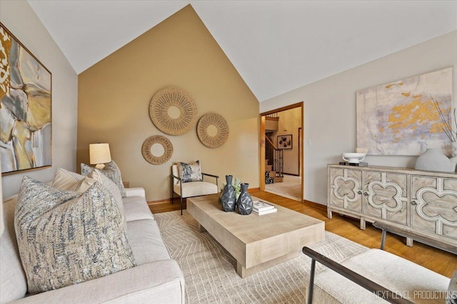 living area featuring stairs, high vaulted ceiling, wood finished floors, and baseboards