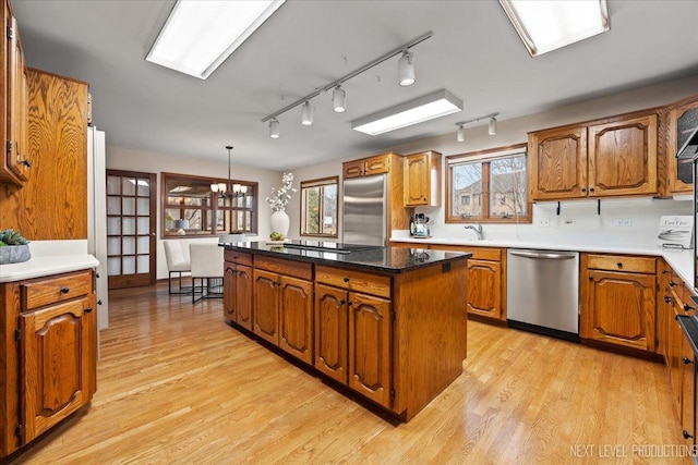 kitchen with an inviting chandelier, appliances with stainless steel finishes, light wood-style floors, brown cabinetry, and a kitchen island