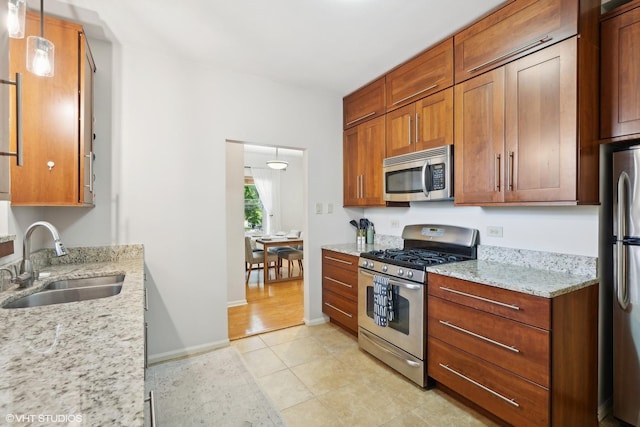 kitchen with light stone countertops, pendant lighting, stainless steel appliances, sink, and light tile patterned floors