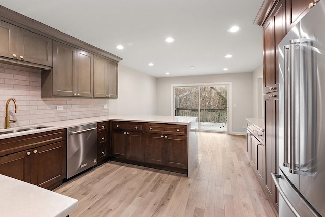 kitchen with sink, light hardwood / wood-style flooring, appliances with stainless steel finishes, backsplash, and dark brown cabinetry