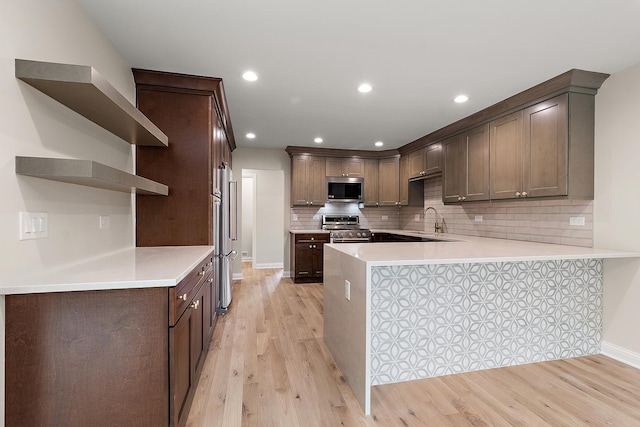 kitchen with sink, light hardwood / wood-style flooring, high quality appliances, decorative backsplash, and kitchen peninsula