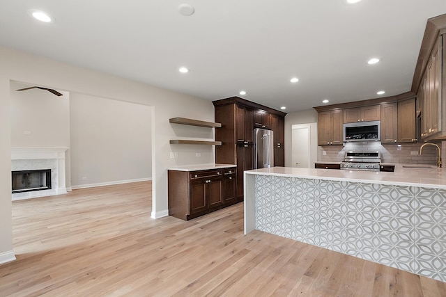 kitchen with sink, light hardwood / wood-style flooring, appliances with stainless steel finishes, a high end fireplace, and kitchen peninsula