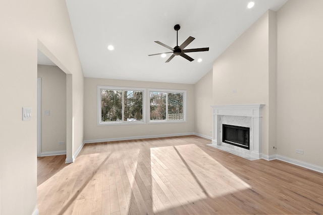 unfurnished living room with ceiling fan, a high end fireplace, high vaulted ceiling, and light wood-type flooring