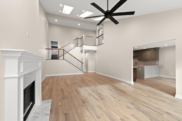 unfurnished living room with sink, light wood-type flooring, ceiling fan, a fireplace, and a high ceiling