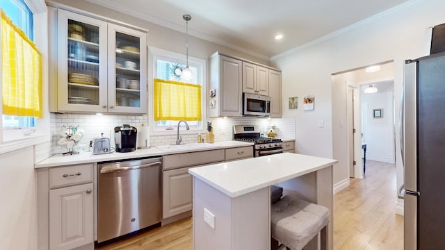 kitchen with sink, hanging light fixtures, appliances with stainless steel finishes, a kitchen breakfast bar, and a kitchen island