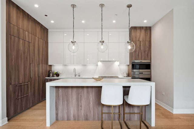 kitchen with white cabinetry, hanging light fixtures, multiple ovens, sink, and light hardwood / wood-style flooring