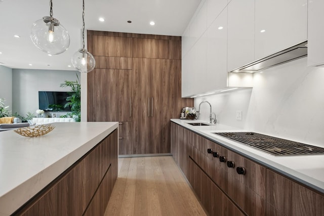 kitchen with decorative light fixtures, sink, white cabinets, exhaust hood, and light hardwood / wood-style floors