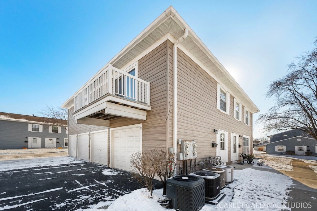 view of snow covered exterior with a garage, central AC, and a balcony