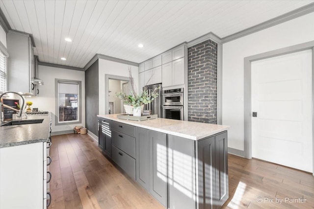 kitchen featuring appliances with stainless steel finishes, sink, gray cabinetry, a center island, and crown molding