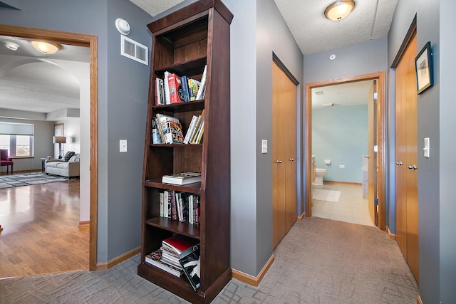 hall featuring light colored carpet and a textured ceiling