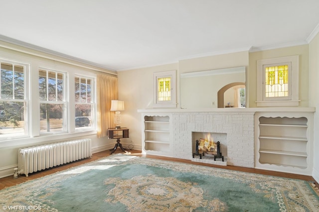 living room with wood finished floors, baseboards, ornamental molding, a brick fireplace, and radiator