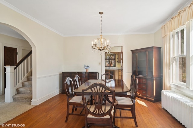 dining room featuring arched walkways, a notable chandelier, radiator, wood-type flooring, and stairway