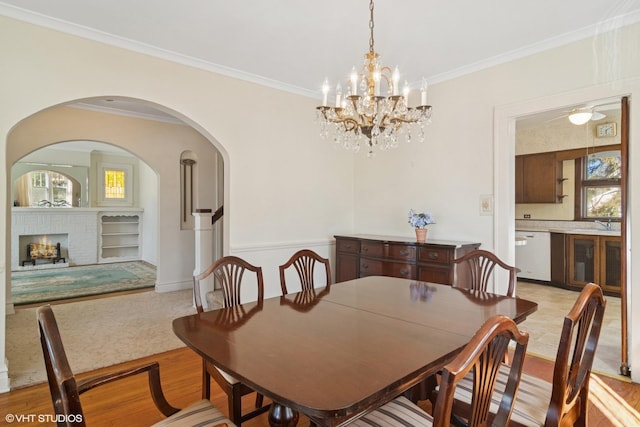 dining space with light wood finished floors, a fireplace, ornamental molding, and arched walkways