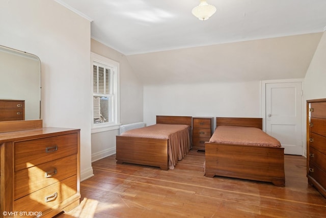 bedroom with radiator, light wood finished floors, baseboards, and vaulted ceiling