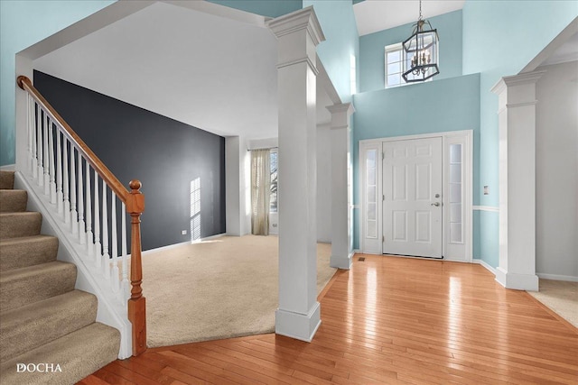 entrance foyer with decorative columns, a towering ceiling, a notable chandelier, and light hardwood / wood-style floors