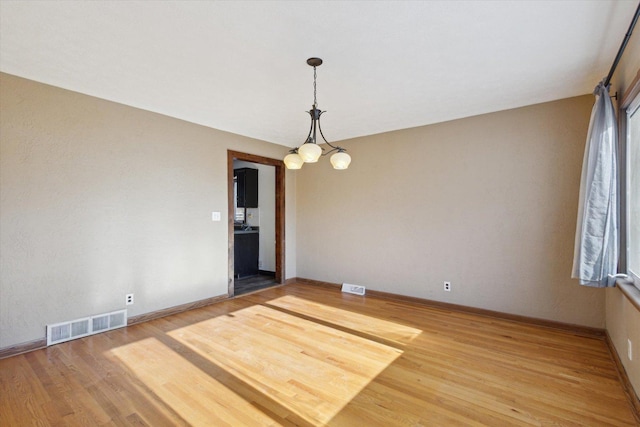 spare room with a notable chandelier and hardwood / wood-style floors