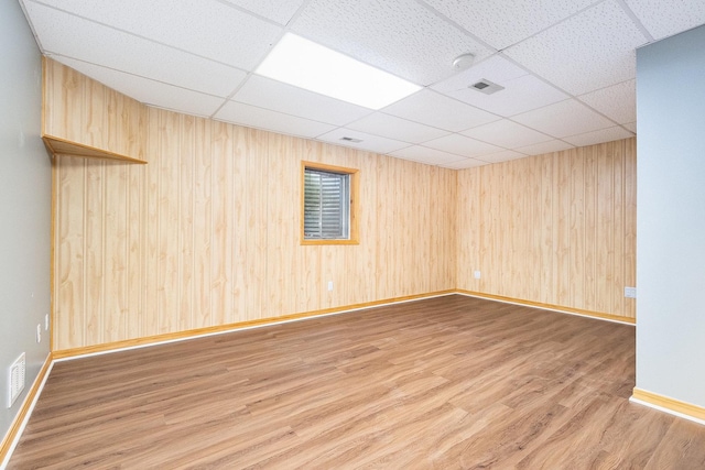 unfurnished room with a drop ceiling, hardwood / wood-style floors, and wooden walls