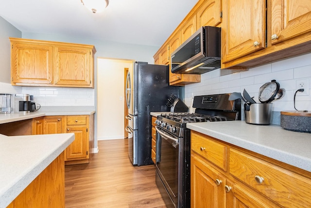 kitchen featuring decorative backsplash, stainless steel fridge, gas range oven, and light hardwood / wood-style flooring