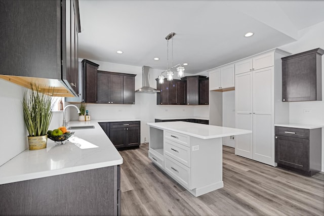 kitchen featuring white cabinetry, sink, a center island, wall chimney range hood, and light hardwood / wood-style flooring