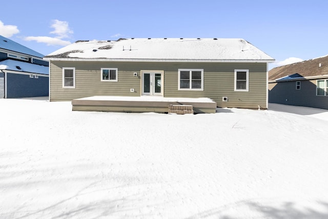 snow covered house with a wooden deck and french doors