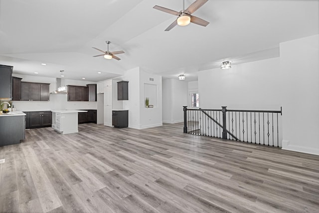 unfurnished living room with sink, light hardwood / wood-style flooring, ceiling fan, and vaulted ceiling