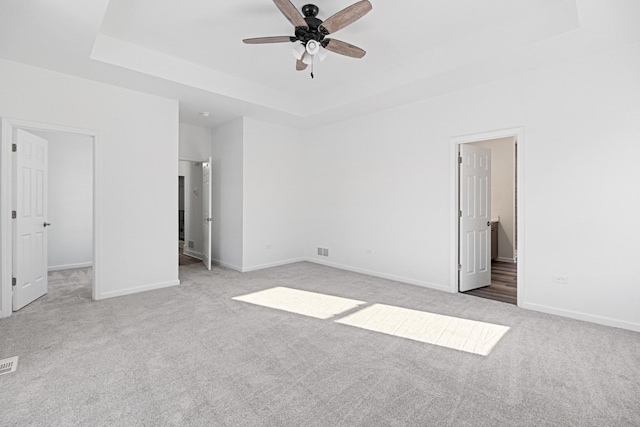 unfurnished bedroom featuring light carpet, connected bathroom, a tray ceiling, and ceiling fan