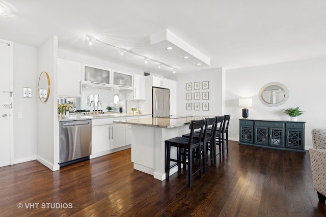 kitchen with dark wood-type flooring, a center island, a kitchen breakfast bar, stainless steel appliances, and white cabinets