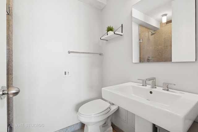 bathroom featuring tiled shower, toilet, and sink