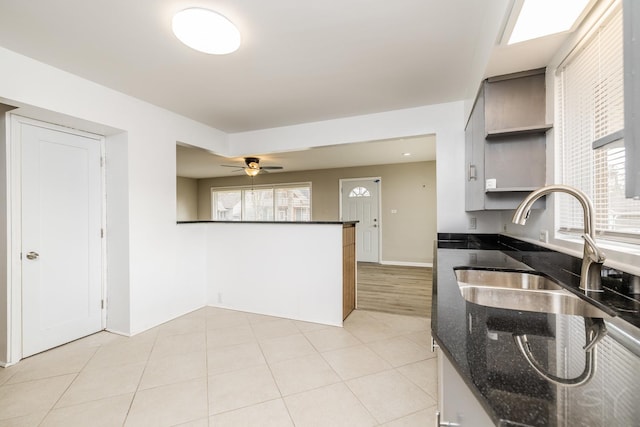 kitchen with light tile patterned flooring, sink, dark stone countertops, and a healthy amount of sunlight