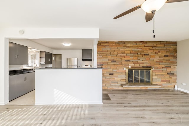 kitchen with ceiling fan, gray cabinetry, fridge, light hardwood / wood-style floors, and a large fireplace