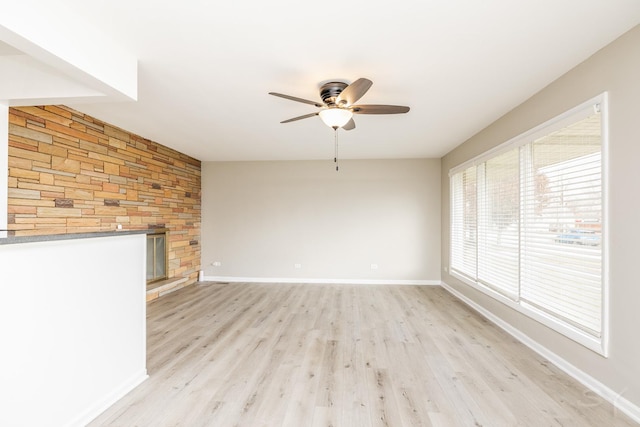 unfurnished living room with ceiling fan, a large fireplace, and light wood-type flooring