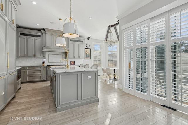 kitchen with hanging light fixtures, a kitchen island with sink, backsplash, and gray cabinets