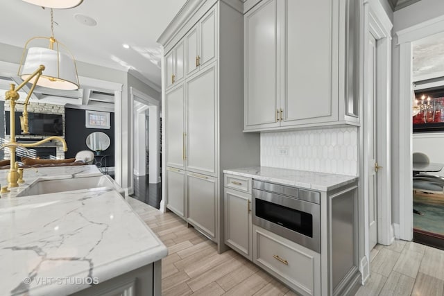 kitchen with sink, gray cabinetry, crown molding, stainless steel microwave, and light stone countertops