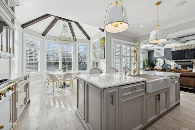 kitchen with gray cabinets, pendant lighting, beamed ceiling, sink, and a kitchen island with sink