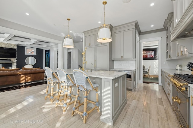 kitchen with a breakfast bar area, gray cabinetry, decorative light fixtures, an island with sink, and light stone countertops