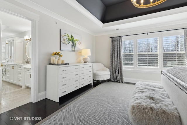 bedroom with a raised ceiling, ornamental molding, connected bathroom, and dark hardwood / wood-style flooring