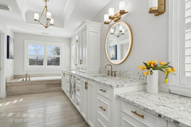 bathroom featuring vanity, tiled tub, a raised ceiling, and an inviting chandelier