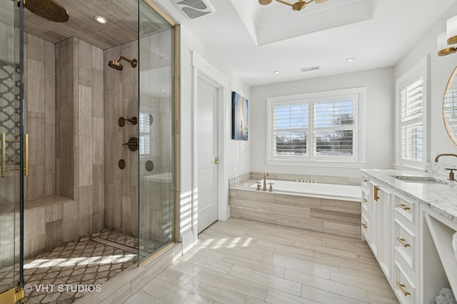 bathroom with vanity, a tray ceiling, shower with separate bathtub, and ceiling fan