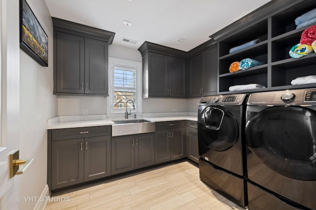 clothes washing area with sink, cabinets, washing machine and clothes dryer, and light wood-type flooring