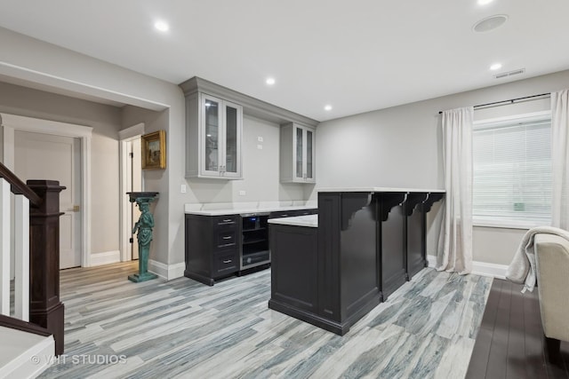 kitchen with light hardwood / wood-style floors, beverage cooler, kitchen peninsula, and a kitchen bar