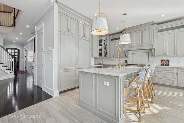 kitchen featuring gray cabinets, pendant lighting, backsplash, light stone countertops, and a center island with sink