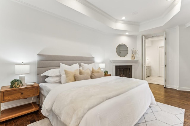 bedroom featuring ornamental molding, connected bathroom, a raised ceiling, and light hardwood / wood-style floors