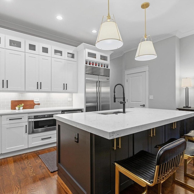 kitchen featuring appliances with stainless steel finishes, white cabinetry, ornamental molding, an island with sink, and decorative light fixtures