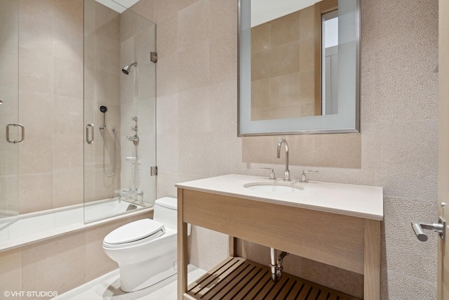 full bath with toilet, a sink, tiled shower / bath combo, and tile walls